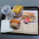Tray with burger, fries, drink, and ketchup package with black markings.
